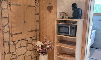 A cozy hallway with a stone wall and a wooden shelf. On the shelf are a microwave and a vase with flowers.