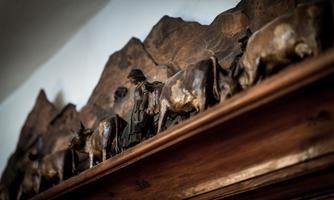 An artistic wood carving depicts a group of cows and a figure accompanying them. Mountainous shapes can be seen in the background.