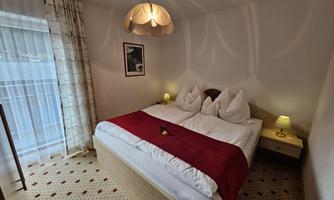 A cozy bedroom with a double bed and two nightstands. The atmosphere is warm and inviting, with a red throw and soft lighting.