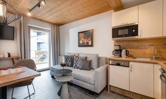 A modern living and dining room with a light wooden ceiling. The kitchen is well-equipped, and a cozy seating area invites you to relax.