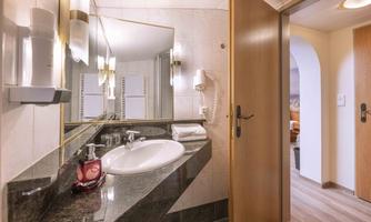 A modern bathroom with a sink, a large mirror, and an elegant granite floor. In the background, an open door to another room is visible.