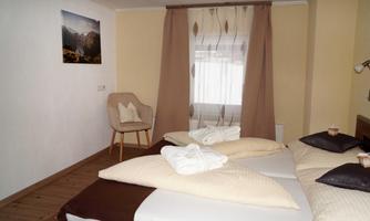 A cozy bedroom with two beds, equipped with blankets and pillows. A chair and a window with curtains complete the inviting atmosphere.