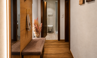 A modern hallway with wooden elements and a cozy bench. In the background, access to the bathroom is visible.