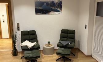 Two cozy armchairs in a modern room, with an artistic picture on the wall. In the middle stands a small table with a plant.