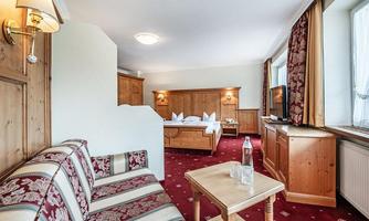 A cozy room with wooden paneling and a floral sofa. In the background, a double bed and a television are visible.
