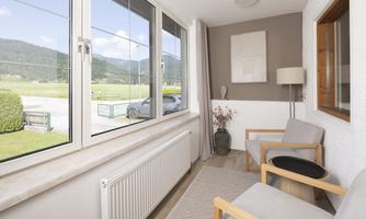 A bright living space with large windows and a view of green countryside. Two comfortable chairs and a lamp create a cozy atmosphere.