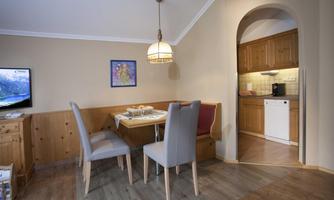 A cozy dining area with a table and chairs in a modern space. In the background, a well-equipped kitchen is visible.