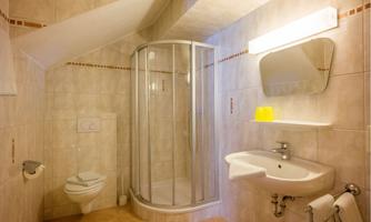 A modern bathroom with a shower, sink, and toilet. The walls are tiled and the lighting creates a bright atmosphere.