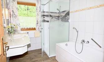 A modern bathroom with a shower and a bathtub. Large windows offer a view of the green surroundings.