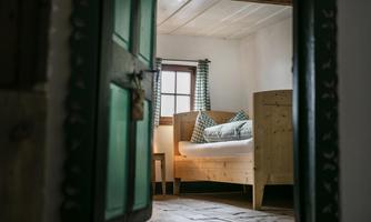 A simple bedroom with wooden beds and checkered cushions. Light falls through a window, creating a cozy atmosphere.