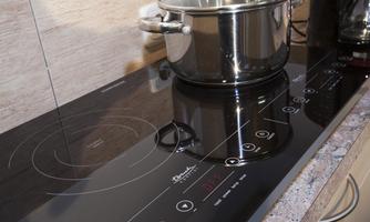 A modern induction cooktop with a stainless steel pot on it. The user interface displays digital controls for the heat.