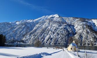A snowy landscape with high mountains in the background. In the foreground, there is a narrow path and a small chapel.