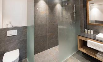 A modern bathroom with a spacious, glass shower and elegant tiles. The washing area is equipped with wood and white towels.