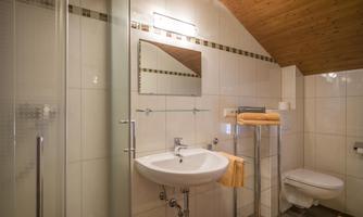 A modern bathroom with a shower cubicle and a sink. The walls are brightly tiled and the ceiling is made of wood.