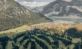 A picturesque landscape with gentle hills, dense forests, and a small village in the background. In the background, majestic mountains and a sparkling lake can be seen.