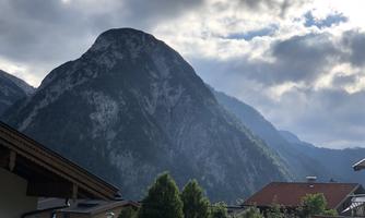 A majestic mountain under a cloudy sky. In the foreground, houses and lush greenery can be seen.