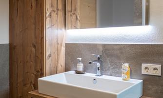 A modern bathroom with a wooden shelf and an elegant sink. The lighting creates a pleasant atmosphere.
