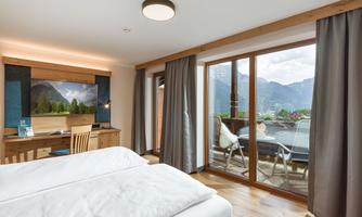 A modern hotel room with a large window that offers a view of the mountains. The decor is bright and inviting, with wooden details and a desk.