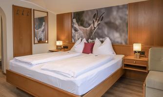 A cozy hotel room with a large double bed and nature-inspired decorations. On the wall hangs a picture of a chamois.