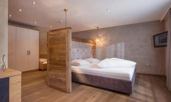 A modern bedroom with a double bed and warm wooden details. There is a small room divider and soft lighting for a cozy atmosphere.