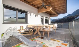 A cozy balcony with a wooden porch and a dining table. A slide and a colorful play rug invite you to play.
