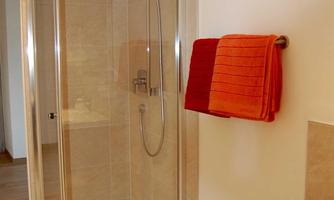 A modern shower with glass partition and a showerhead. Next to the shower hang two orange towels.