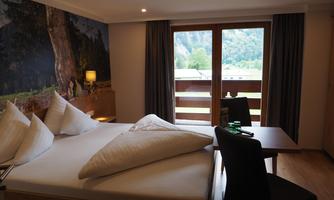 A cozy hotel room with a double bed and a desk. Large windows offer a view of nature outside.