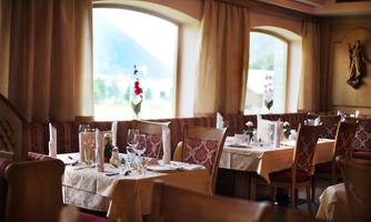A cozy restaurant with tablecloths, glasses, and flowers on the tables. Large windows provide a view of the surrounding scenery.