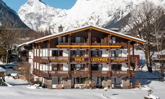 A cozy house in the snow with a view of majestic mountains. The facade is made of wood and has an inviting character.