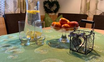 A table setting with a green tablecloth, on which a pitcher of lemon water and glasses are placed. In the background, apples and a decorative lantern are visible.