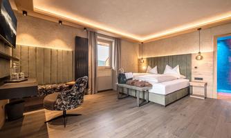 A modern hotel room with a large bed and a cozy armchair. Soft lighting and wooden flooring create an inviting atmosphere.