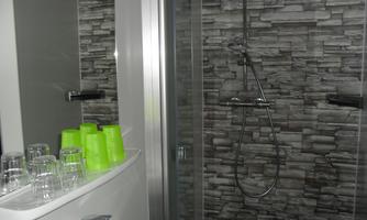 A modern bathroom with a shower and a stone wall. On the shelf are green glasses and a sink faucet.