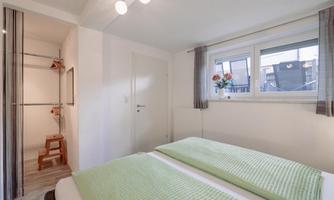 A cozy bedroom with two single beds and green bed covers. The room has large windows that let in plenty of daylight.