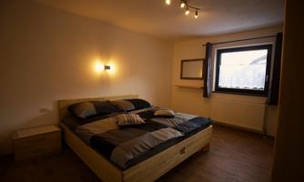A cozy bedroom with a large bed and modern lighting. The window lets in plenty of natural light and the walls are kept neutral.