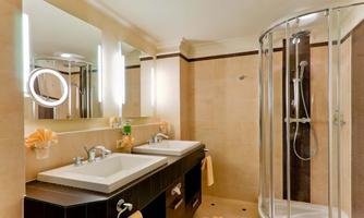 A modern bathroom with two sinks and large mirrors. The shower is separated by a glass door, and the walls are in soft beige and brown tones.
