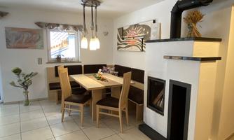 A cozy dining area with a wooden table and chairs. Pictures hang on the wall, and a fireplace creates a pleasant atmosphere.