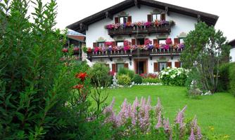 A charming building in alpine style with blooming balconies. The garden is lush and colorful.
