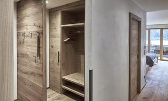 A modern room with wooden paneling and an open wardrobe. Light pours in through large windows, creating a bright atmosphere.