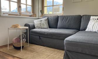 A cozy living area with a gray sofa and a small side table. Large windows offer a view of the mountains.