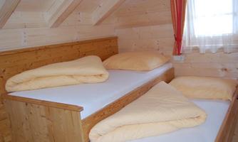 A cozy bedroom with two single beds and yellow bedding. The walls are made of wood, and a window lets in daylight.