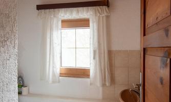 A simple bathroom with a toilet and a window. The walls are light and there is a carpet in front of the toilet.