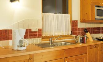 A cozy kitchen with wooden cabinets and a sink. On the countertop, there is a kettle and various cooking utensils.
