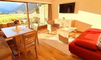 A modern living room with a red sofa and a wooden table. Large windows offer a view of the mountains and let in plenty of daylight.