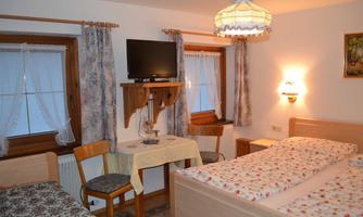 A cozy room with two beds, a table, and a TV. Bright curtains and a lamp create a pleasant atmosphere.