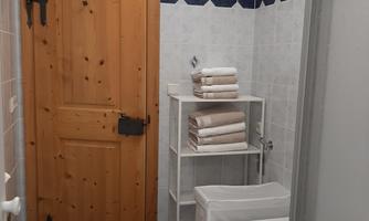 A bathroom with a wooden staircase and a bathtub. Fresh towels are neatly stacked on a shelf.