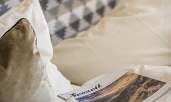A cozy bed with soft pillows and a magazine on the blanket. The colors are neutral and create a relaxed atmosphere.