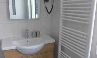 A modern bathroom with a sink, a mirror, and a towel warmer. The walls are brightly tiled and the floor is blue.