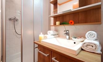 A modern bathroom with a shower and a wooden sink. Clean, folded towels and a candle create an inviting atmosphere.
