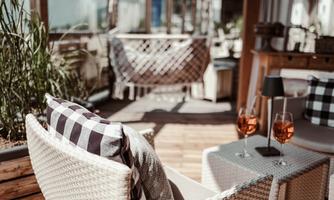 A cozy outdoor area with modern furniture and two glasses of aperitif on a table. The atmosphere is relaxed and inviting.