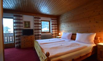 A cozy bedroom with wood paneling and two single beds. Light streams in through the window onto the red-checked curtains and the television.